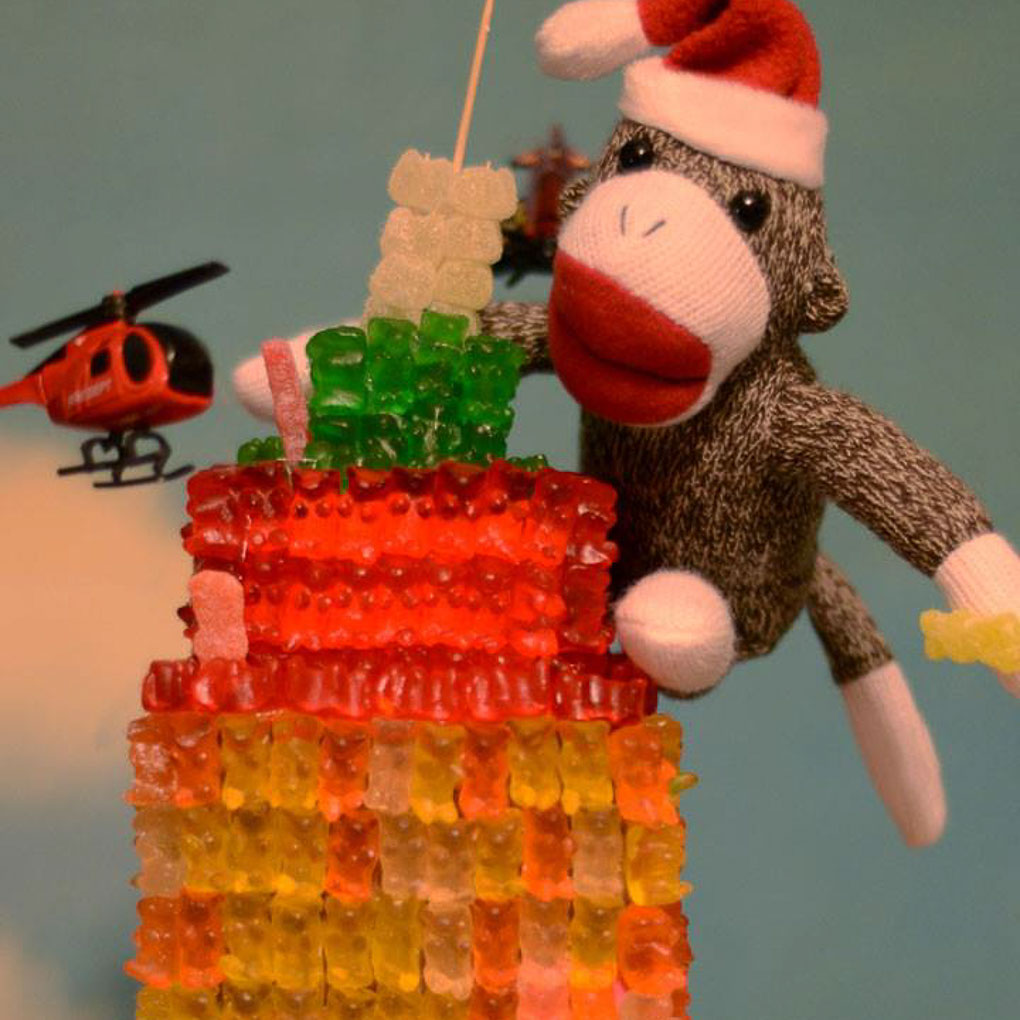 empire state building made out of gummy bears with a sock monkey climbing it and a toy helicopter circling